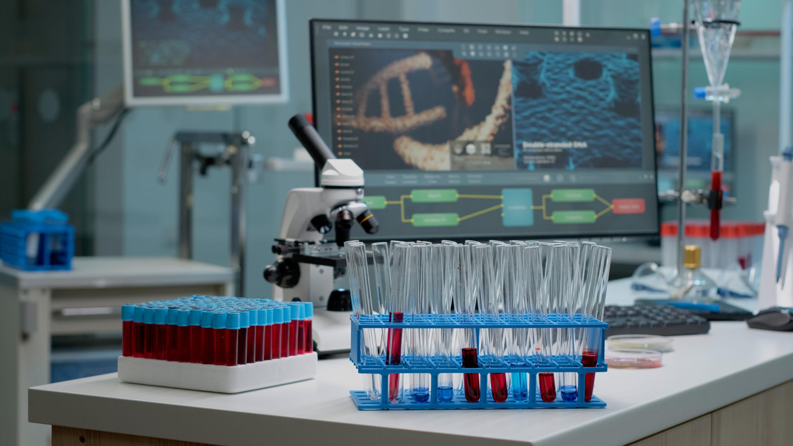 Medical test tubes with blood on desk in laboratory at research clinic. Biotechnology glassware, microscope and pipette as scientific equipment used for discovery in chemistry industry